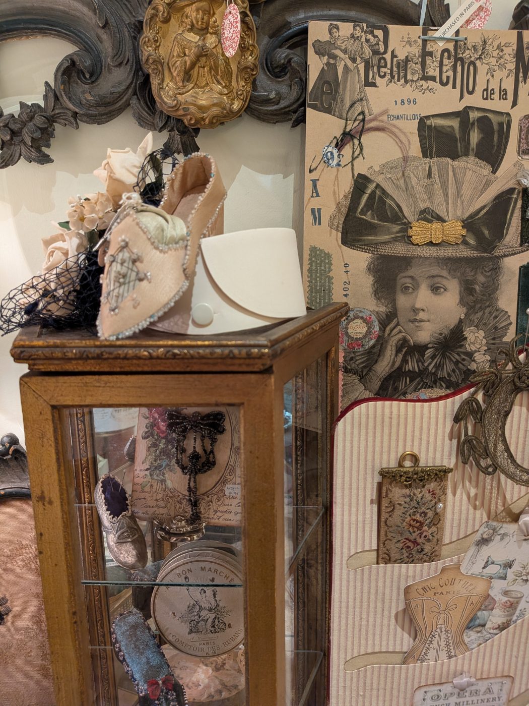 Antique sewing collectibles — pincushion shoes and French millinery in a glass curio