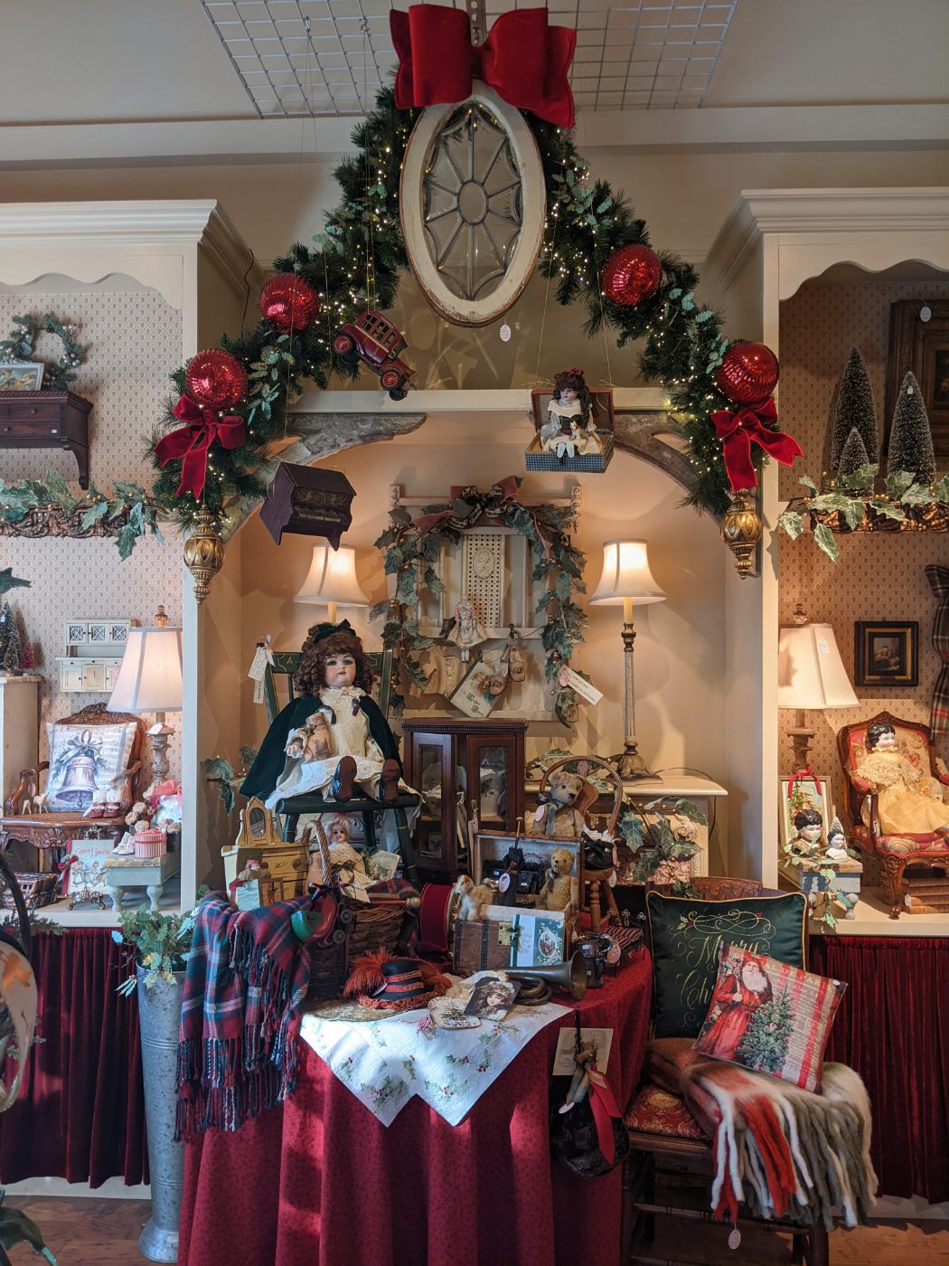 Antique Christmas toys — bisque dolls and teddy bears under a lit garland arch