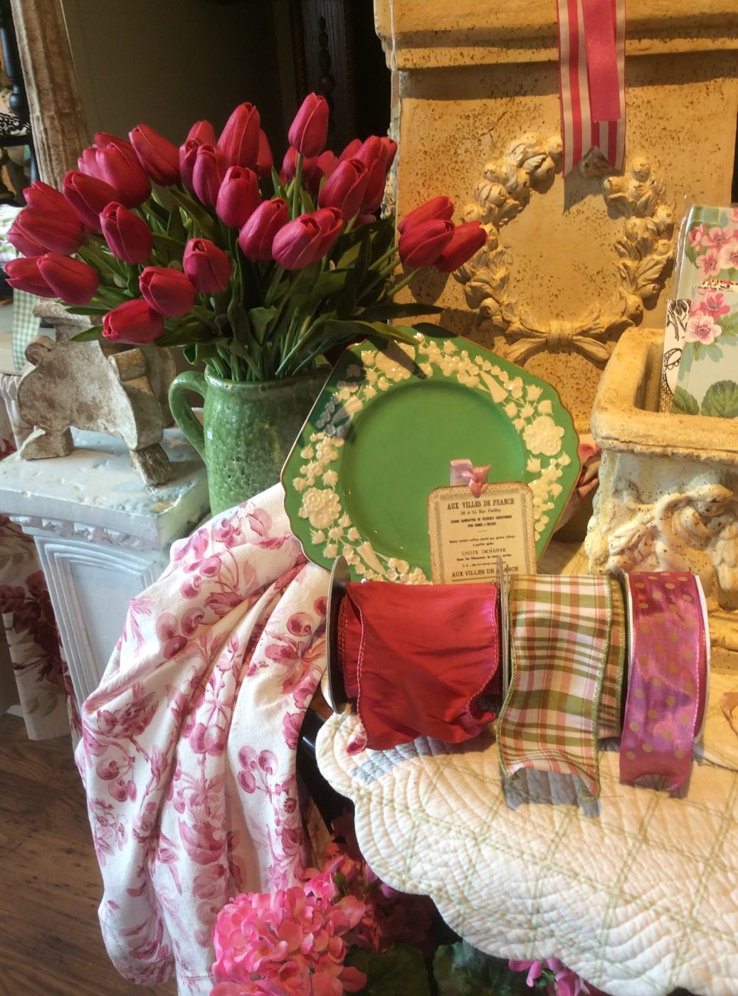 Wired ribbon on spools beside red tulips, a green majolica plate and rose toile